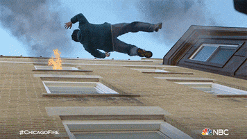 TV gif. Scene from Chicago Fire of a boy falling out of a burning apartment building before being caught by a man. A firefighter assists both on the ground.