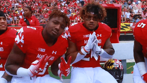 Sports gif. Three football players on the Maryland Terrapins sit on the sidelines. They pose for us, holding out peace signs, holding their hands in a praying position. One of them hugs the other and holds his thumbs up.