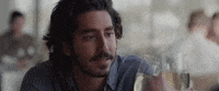 Movie gif. Dev Patel as Saroo in "Lion" clinks champagne glasses with others off-screen and smiles.