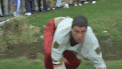 Movie gif. Adam Sandler as Happy Gilmore tackles Bob Barker before they roll down a hill together.