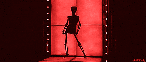 Digital art gif. Silhouette of a sexy skeleton as she dances in front of a red background, stripping off a dress and revealing her hips, ribcage, and skull.