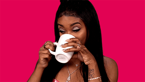 Celebrity gif. Dreezy glances to the side as she holds a white mug and sips daintily with her pinky up. 
