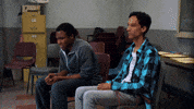 TV gif. Donald Glover as Troy and Danny Pudi as Abed from Community are sitting together waiting nervously. We zoom in on Troy as he begins to rock back and forth intensely, holding his breath and pursing his lips together.