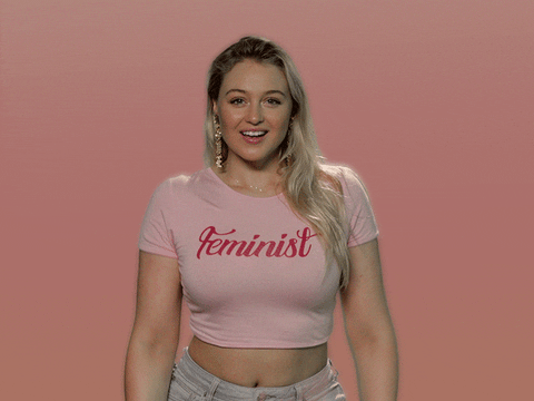 Celebrity gif. Wearing a pink crop T-shirt that says "Feminist," Iskra Lawrence brings both hands to her mouth and blows us a big kiss, opening her arms wide.
