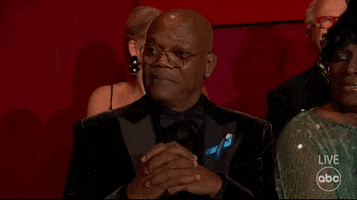 Celebrity gif. Samuel L. Jackson sits in a black tux at the Oscars. He points toward someone as he tilts his head down and raises his eyebrows.