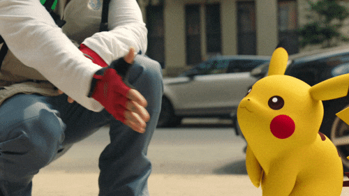 Pokémon gif. Pikachu jumps forward and lands an enthusiastic high five on the hand of a person squatting beside him.