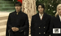 Met Gala 2024 gif. We pan across all 8 members of the K-pop band Stray Kids wearing black wool coats in different styles and button patterns.