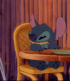 Disney gif. Stitch from Lilo and Stitch sits at a table and looks off to the side, clapping his hands and smiling.