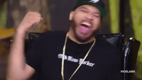 TV gif. Mero on Desus on and Mero. He's sitting in a chair and laughing as he does a happy snap with his hand.