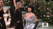 Met Gala 2024 gif. Sydney Sweeney wearing a silvery Miu Miu gown and bold jet-black bobbed wig, drops her chin in slomo, sultry and aloof.