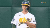 Sports gif. Zack Gelof in a batter's helmet of the Oakland Athletics swipes his arm straight across his chest doing a baseball sign as he nods his head with a frown like, "This is the move."