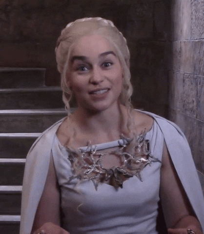 TV gif. Emilia Clarke on Game of Thrones set, dressed as Daenerys, smiles at us and gives us two thumbs up, nodding.