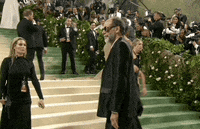 Met Gala 2024 gif. Luca Guadagnino wearing a Loewe suit and bold oversized sunglasses, stands allowing his picture to be taken, landing with a short decisive nod.