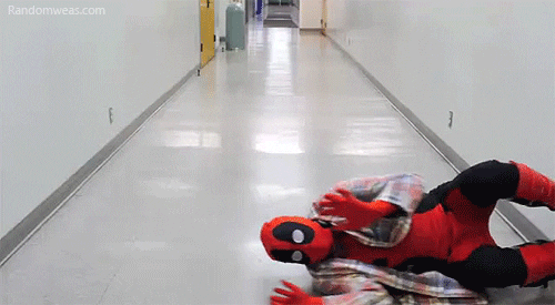 Video gif. Man in a Deadpool costume and a flannel shirt slides himself on the floor of a hallway, kicking his feet off the walls to keep himself sliding continuously on the floor.