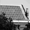 Text gif. Sticker in the style of Barbara Kruger, red with white oblique Futura lettering, reading "Go solar," slaps across a black-and-white photo of a post-medieval English-style urban house with solar panels on the roof.