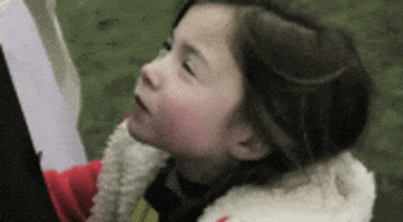 Video gif. A young girl turns to the camera and smirks knowingly.