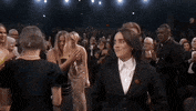 Oscars 2024 GIF. Billie Eilish and Finneas O'Connell walk towards the stage to accept their award for Best Song before Eilish spontaneously diverges to run and hug America Ferrera. 