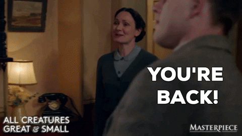 TV gif. Anna Madeley as Mrs. Hall on All Creatures Great and Small walks up to a man with a big, warm smile on her face. She says, “You're back!” and gives him a big hug.