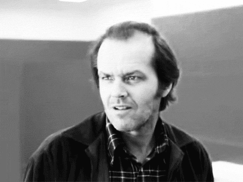 Movie gif. In black and white, Jack Nicholson as Jack Torrance in The Shining smiles with complete madness.