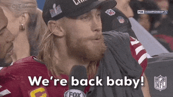 Sports gif. George Kittle of the San Francisco 49ers, declares into a sideline reporter's microphone, "We're back, baby! Wooooo!" Text, "We're back, baby! Woooo!"