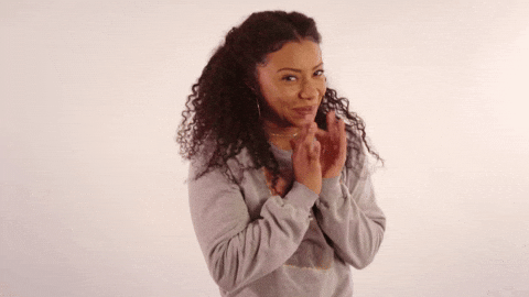 Celebrity gif. Shalita Grant looks cheeky as she smiles sneakily and drums her fingers together.