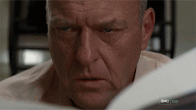 TV gif. Dean Norris as Hank in Breaking Bad looks up from a paper he's reading and realization hits his face. He looks shocked and livid, as he's just figured out something life changing.