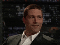 Video gif. Charming young man with a clean buzzcut and a sharp suit smiles and nods quietly in agreement.