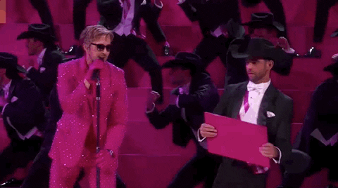 Oscars 2024 GIF. Ryan Gosling is in the middle of his performance for I'm Just Ken and he punches and breaks a wooden panel, yelling out with vigor. Background dancers lean to the right behind him and they're all wearing black cowboy hats and tuxedos.  