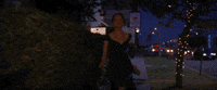 Movie gif. Emma Stone as Mia from La La Land runs down a sidewalk at night with a giddy smile, holding out her dark green dress by the skirt.
