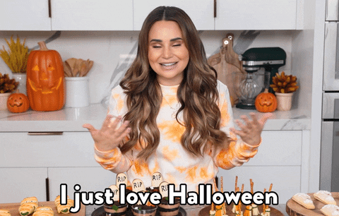Video gif. Rosanna Pansino, a Youtuber, stands at her kitchen table which is filled with Halloween inspired treats. She smiles and shrugs while holding her arms out, saying, "I just really love Halloween."