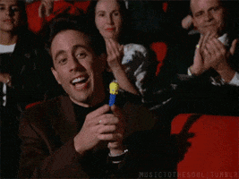 Seinfeld gif. Sitting among an applauding audience, Jerry smiles and taps his pointer fingers while clasping a Tweety Bird Pez dispenser.