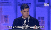 Video gif. Saturday Night Live's Colin Jost stands at a podium at the 2024 White House Correspondents' Dinner as he surveys the room with a sly look and deadpans "Too chilling for you guys?"