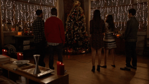 TV gif. Five cast members from New Girl stand facing a brilliantly lit Christmas tree. The lights begin to flicker before the apartment goes dark.