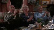 Movie gif. Three elderly people in Groundhog Day sit on a couch in a living room, cups of tea on the table in front of them, clapping politely with slight smiles.