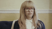 TV gif. Carrie Brownstein on Portlandia wears a blonde wig and big aviator glasses. She looks around and shrugs her shoulders.