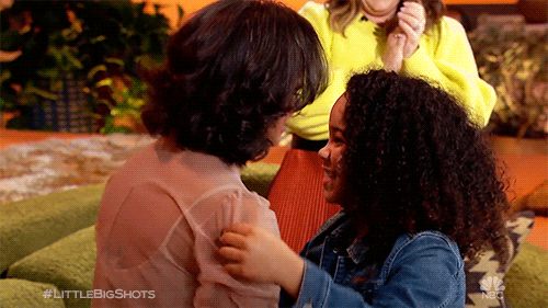 Reality TV gif. A woman and a young girl embrace with big smiles on their faces on Little Big Shots. 