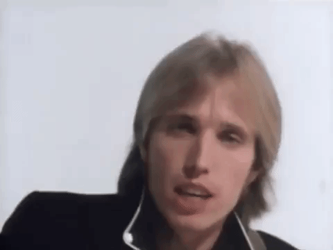 Music video gif. Tom Petty sings as he looks at us, playing a guitar off screen. Text, "Yeah the waiting is the hardest part," with emphasis on the word, hardest. 
