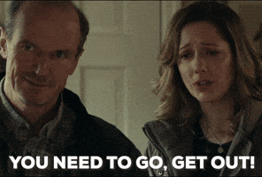 Movie gif. Judy Greer as Karen Nelson in Halloween stands next to her husband at the front door. Shutting the door with a worried look on her face, she says, "You need to go, get out," which also appears as text.