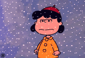 Peanuts gif. Lucy stands outside, frowning and with balled-up fists at her sides, as snow falls down.