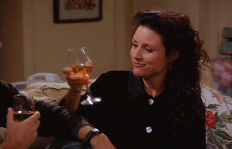 Seinfeld gif. Julia Louis-Dreyfus as Elaine clinks wine glasses with a man and smiles eagerly and dorky, biting her lower lip.
