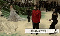 Met Gala 2024 gif. Morgan Spector wearing a red Willy Chavarria ensemble with oversized flowers, stands for the cameras, striking a pose with sweet smugness.
