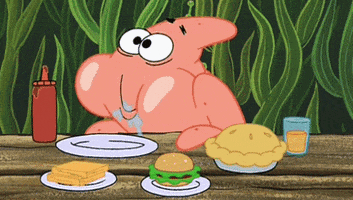 SpongeBob gif. Patrick happily chews with big bulging cheeks and saliva all over his mouth. He leans over a table that has an empty plate and various foods on it.