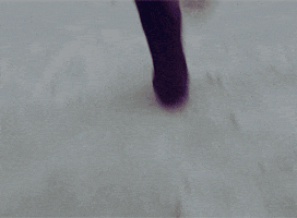 TV gif. Sneakers run through the sand, revealed to be Radha Mitchell as Marta Walraven from Red Widow having a refreshing jog along a cloudy beach, as she listens to music with wired earbuds.