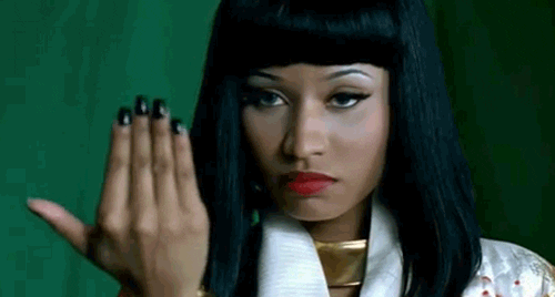 Celebrity gif. Nicki Minaj glares menacingly ahead. She closes the fingers of her outstretched hand as if signaling, bring it on.