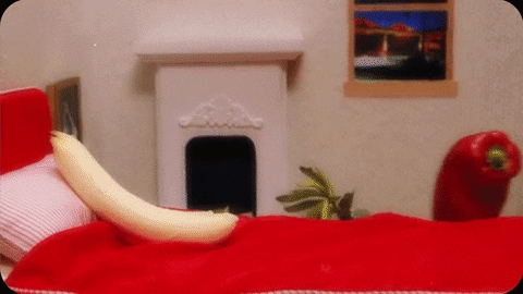 Video gif. Peeled banana lays on a bed as a red pepper and squash slide in. Hands then play with the three fruits like they’re having sex, jostling the banana and squash against the pepper. Suddenly a corn on the cob and two long carrots join in. As the fruits and veggies have their orgy, a cucumber walks in on them and a potato peeks through the window.