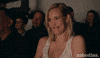 TV gif. Among an audience, on the show Nobodies, Leslie Bibb as Sam snickers quietly, raising her hand to cover her mouth.