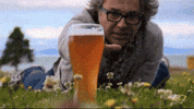 Video gif. Man lies in a meadow, desperately reaching for a glass of beer before it suddenly disappears, leaving him devastated.