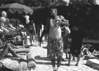 Celebrity gif. Black and white clip of Will Smith purposefully falling into an empty lounge chair next to a beautiful woman at a pool.