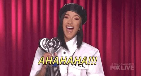 Celebrity gif. Cardi B holds an iHeartRadio award and leans back, cackling.