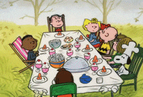 Cartoon gif. Characters in Charlie Brown Thanksgiving sit around a table full of food in the backyard of someone’s house. Linus stands up and everyone looks at him as he speaks.